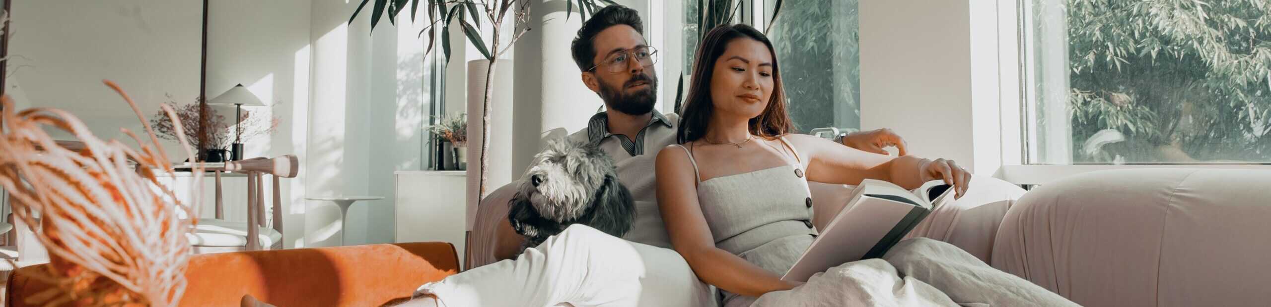 man with dog sitting on couch with woman reading a book