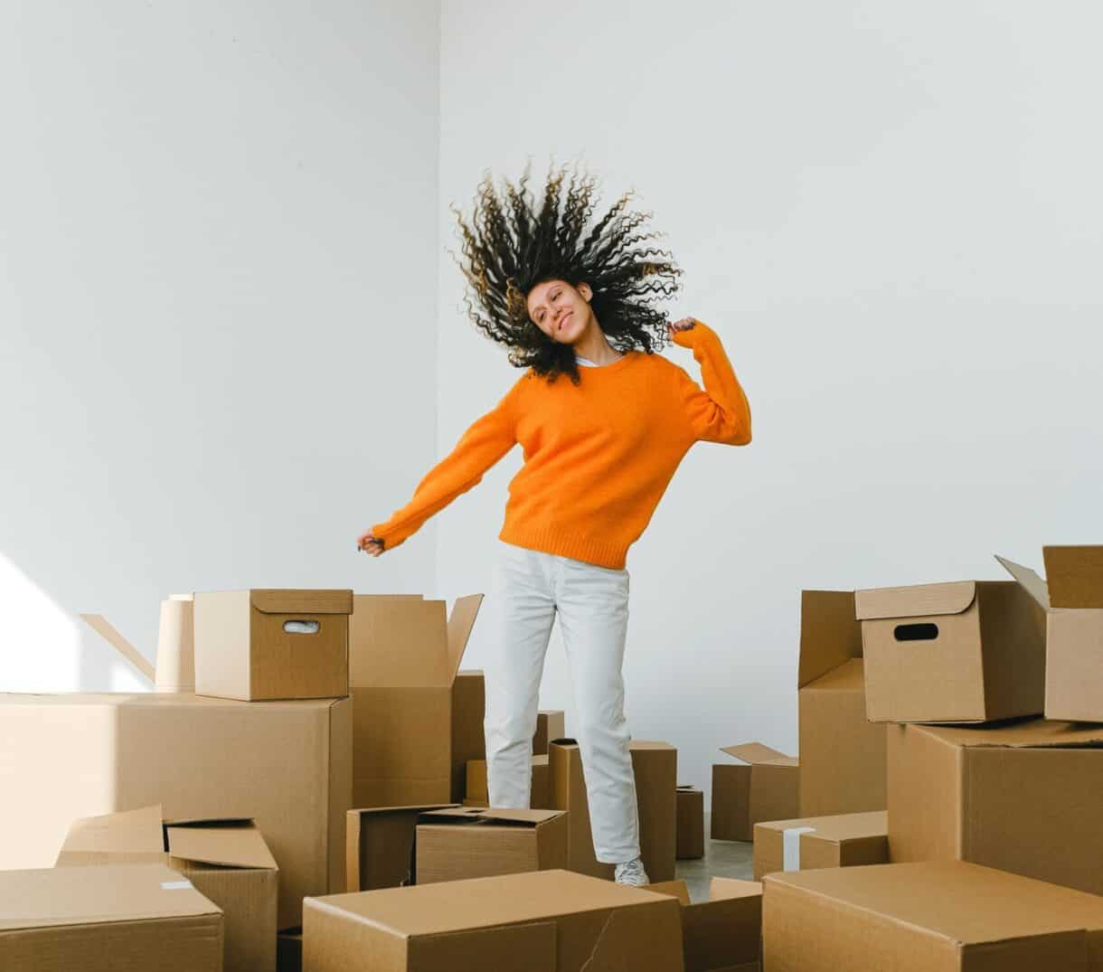 woman in orange shirt jumping with hair straight up surrounded by moving boxes