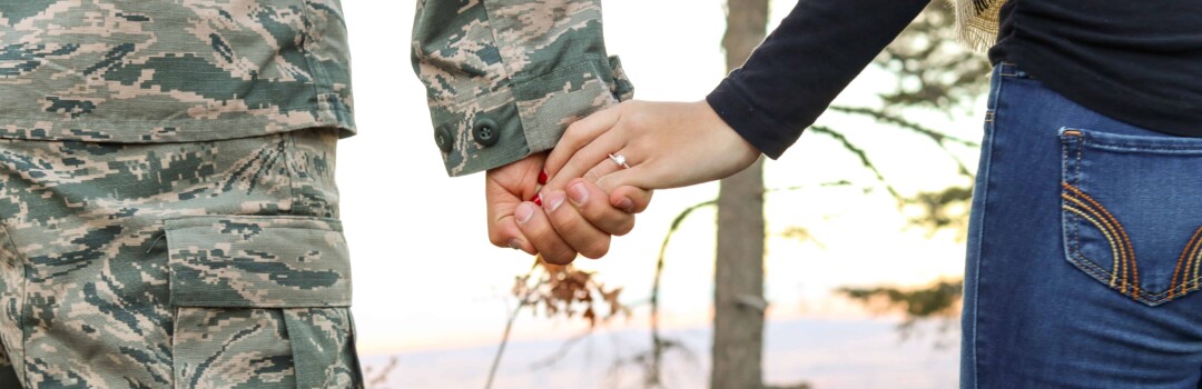 man in army uniform holding woman's hand with engagement ring